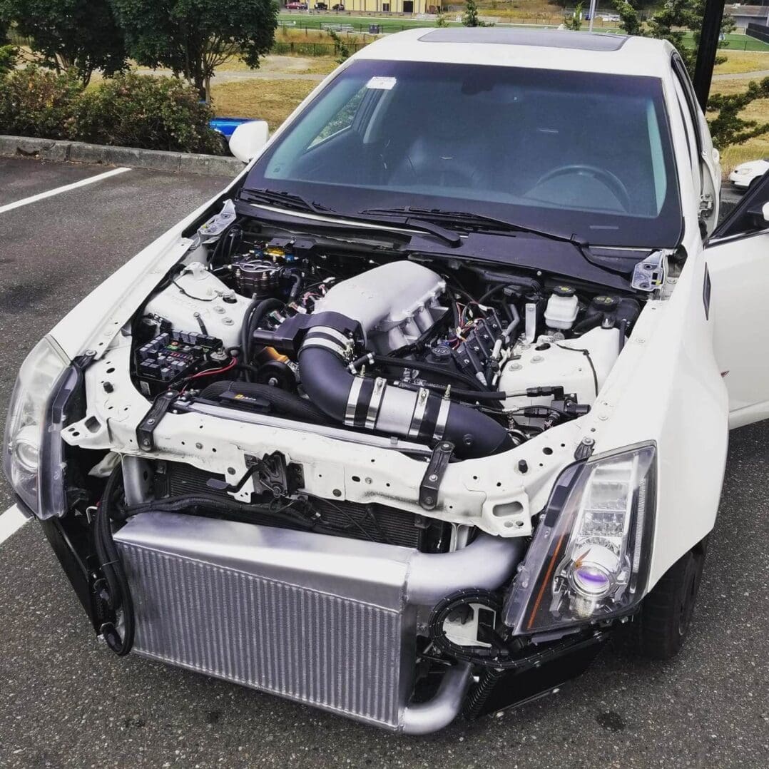 White car with front bumper removed, exposing engine and radiator.