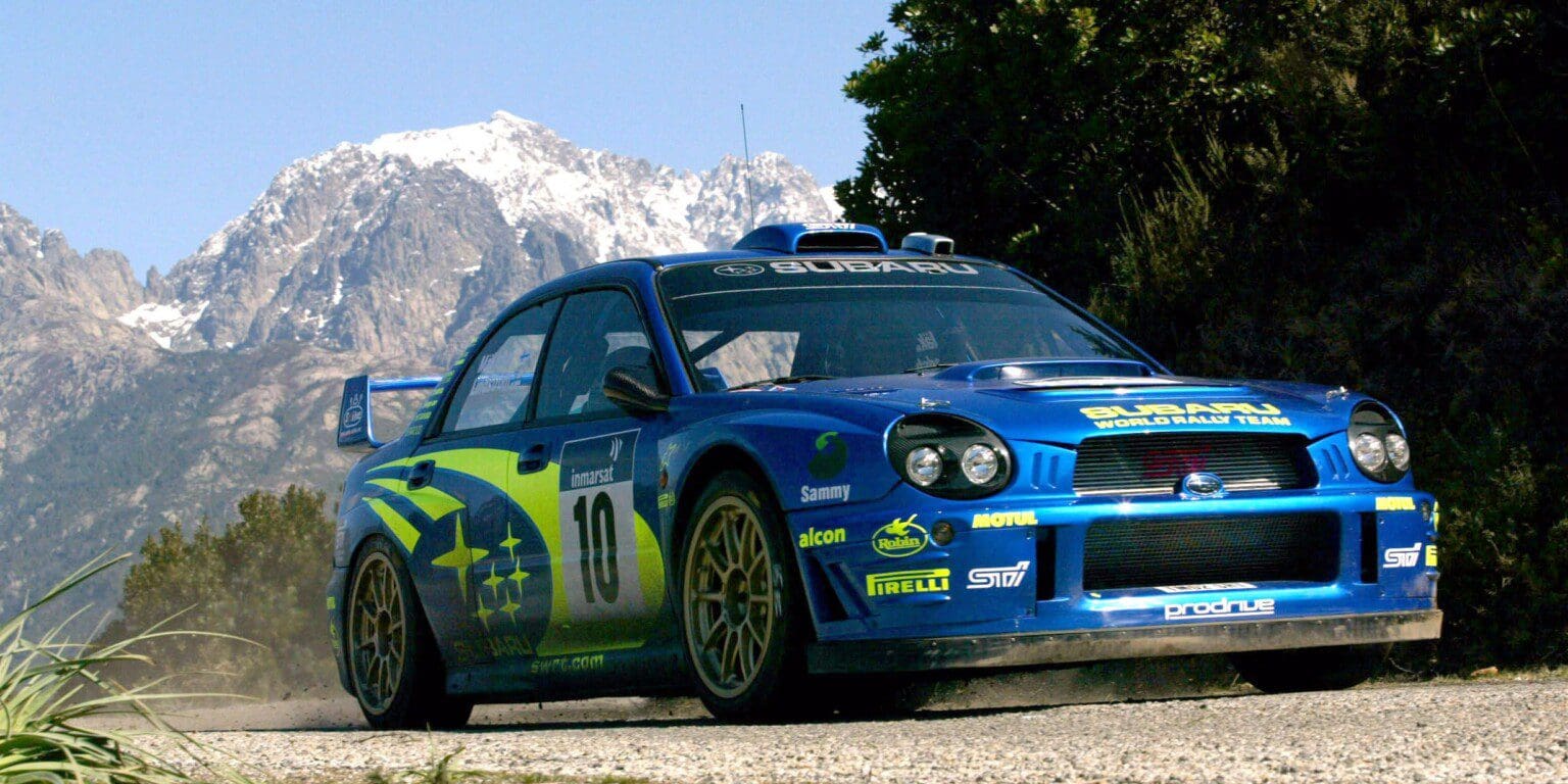 A blue Subaru rally car with green decals on a mountain road.