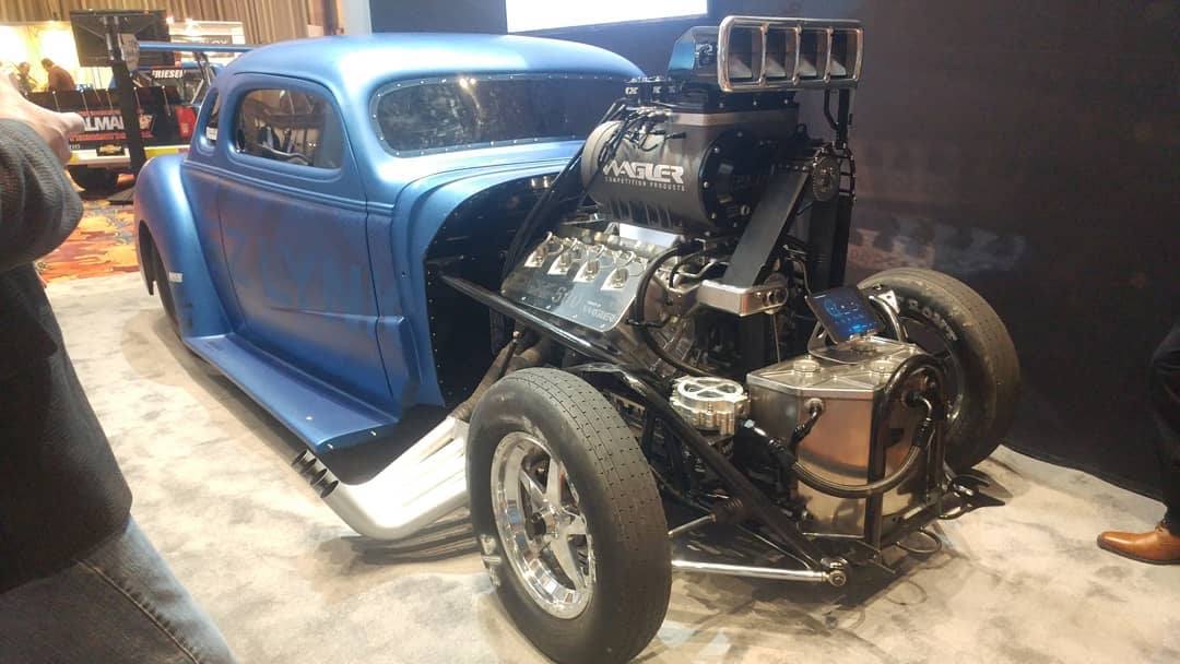A blue hot rod car with a powerful exposed engine in a garage.