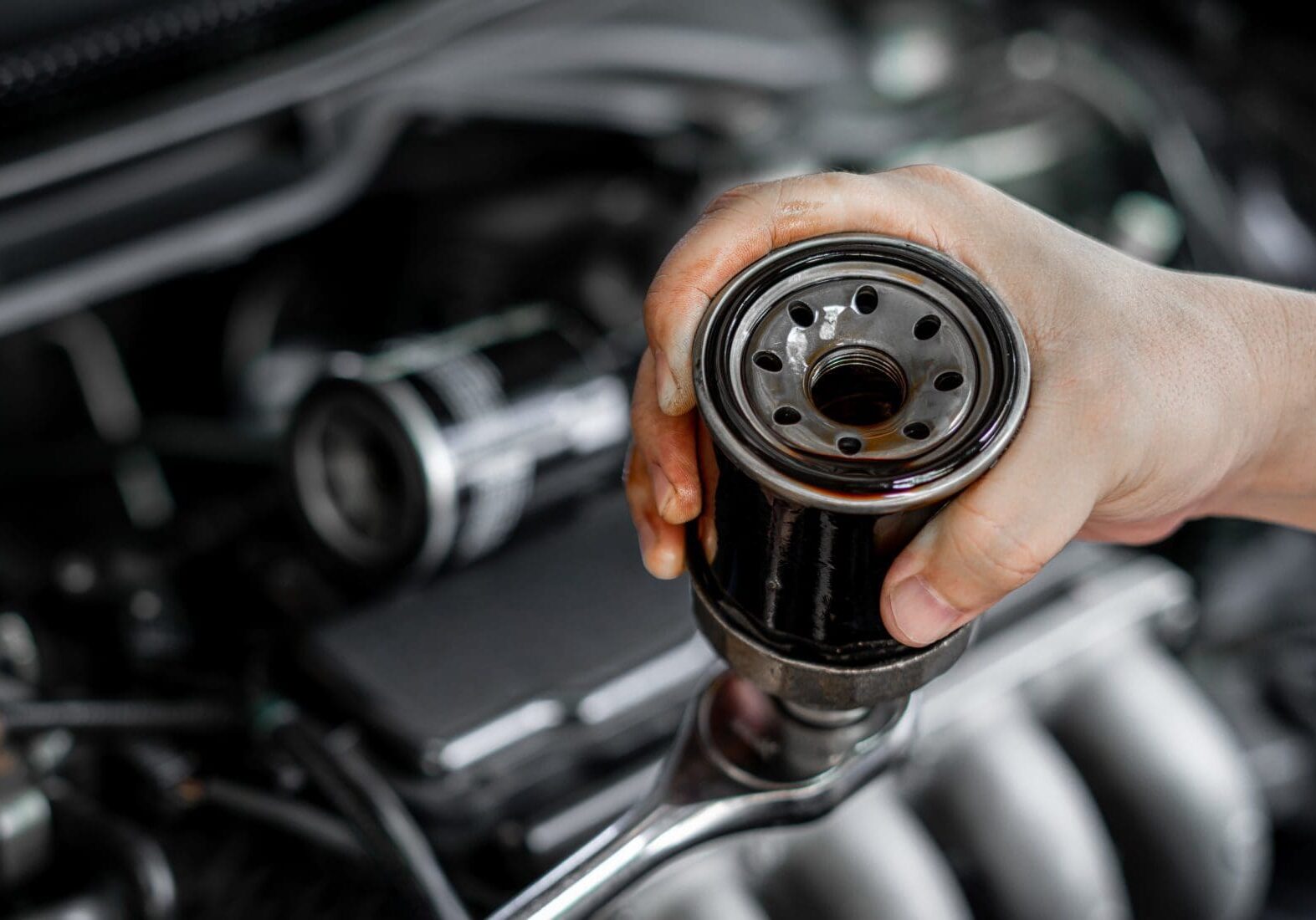 Person holding a car oil filter above an engine.