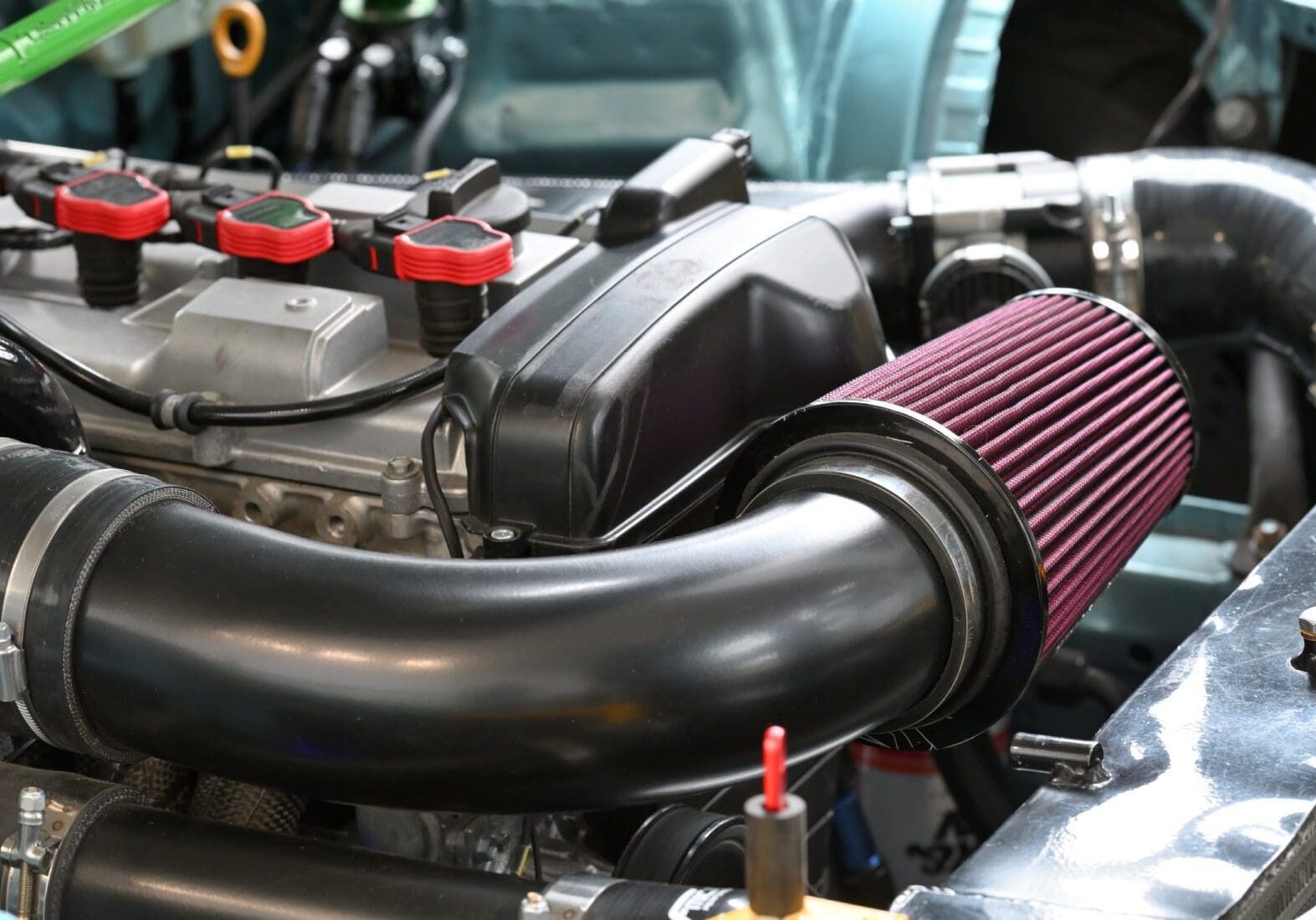 Close-up of a car engine showcasing a red cone air filter, black intake pipe, and partially visible engine components.